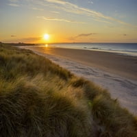 Sunce koje se odražava na travi dine na plaži na izlasku sunca nad sjevernim morem u Bamburghu u Northumberlandu,